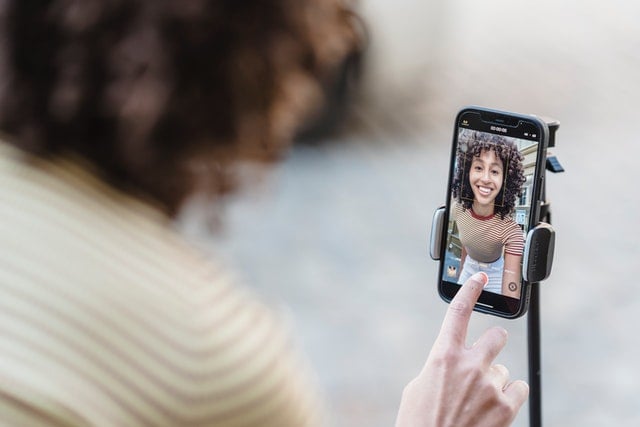 Woman smiling into camera and about to press play with phone on tripod.